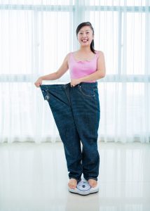 Young woman standing on a measuring scale and showing her success after losing weight.
